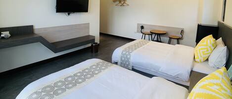 A hotel room with two beds, a TV mounted on the wall, a small table, and a chair.