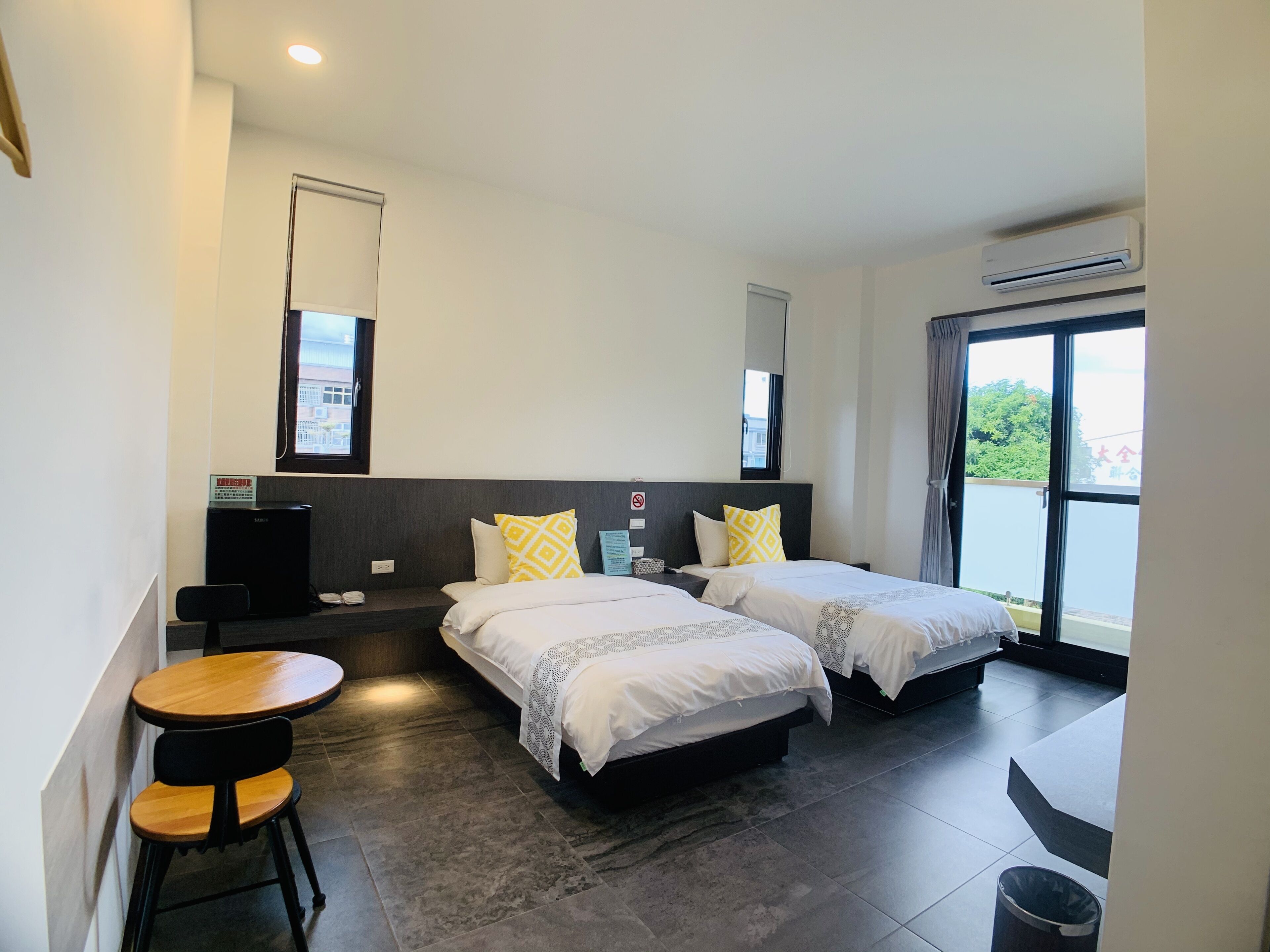 A hotel room with two beds, a small table with chairs, a desk, and a trash bin.