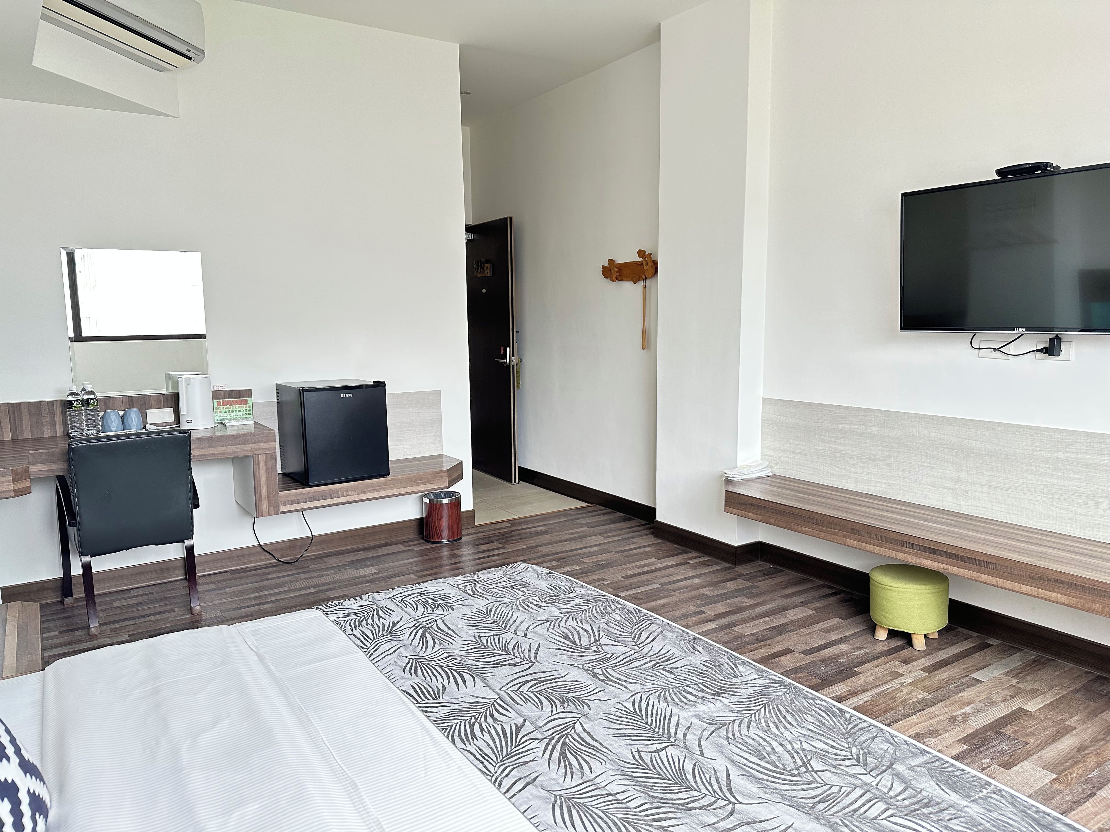 Habitación de hotel con cama, escritorio, computadora, televisor y una pequeña zona de estar.