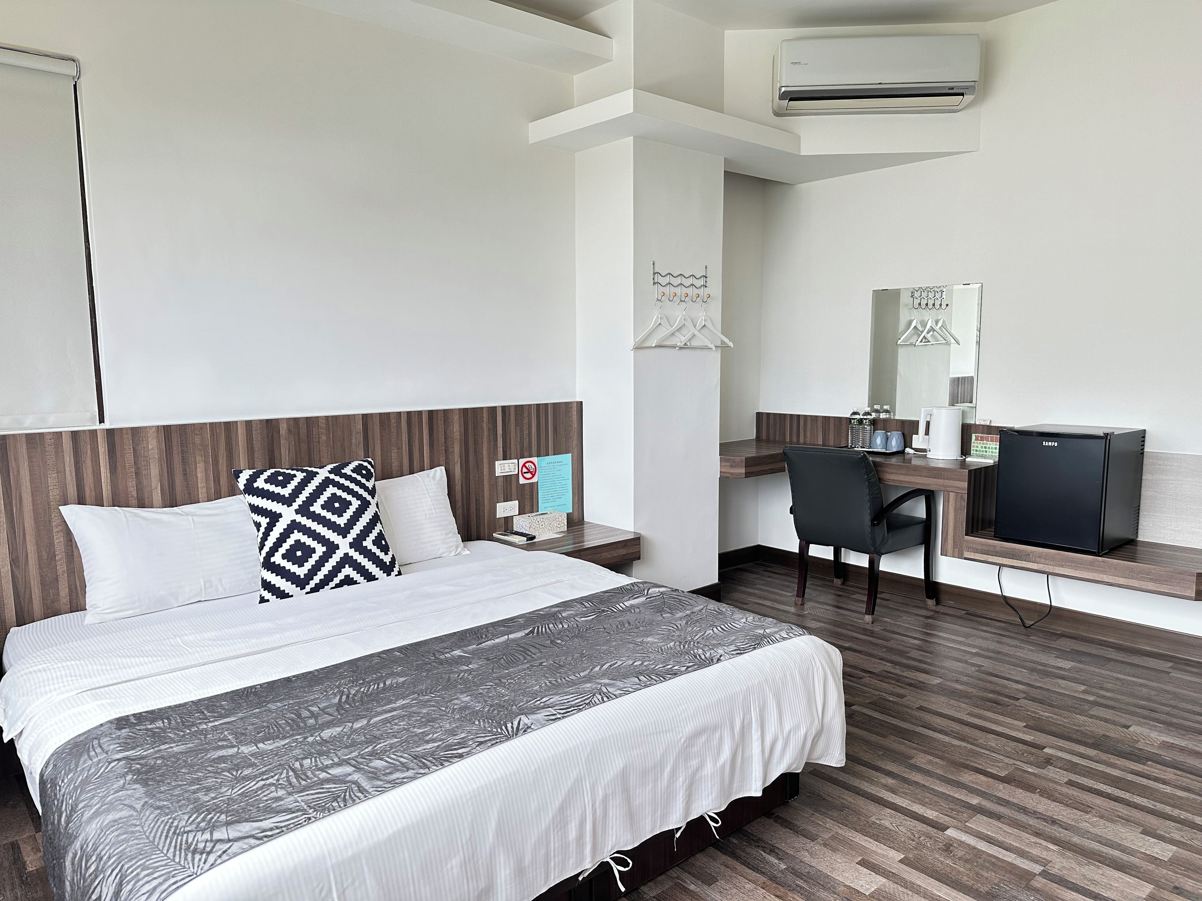 A hotel room with a bed, a desk, a chair, a minibar, and a wall-mounted air conditioner.