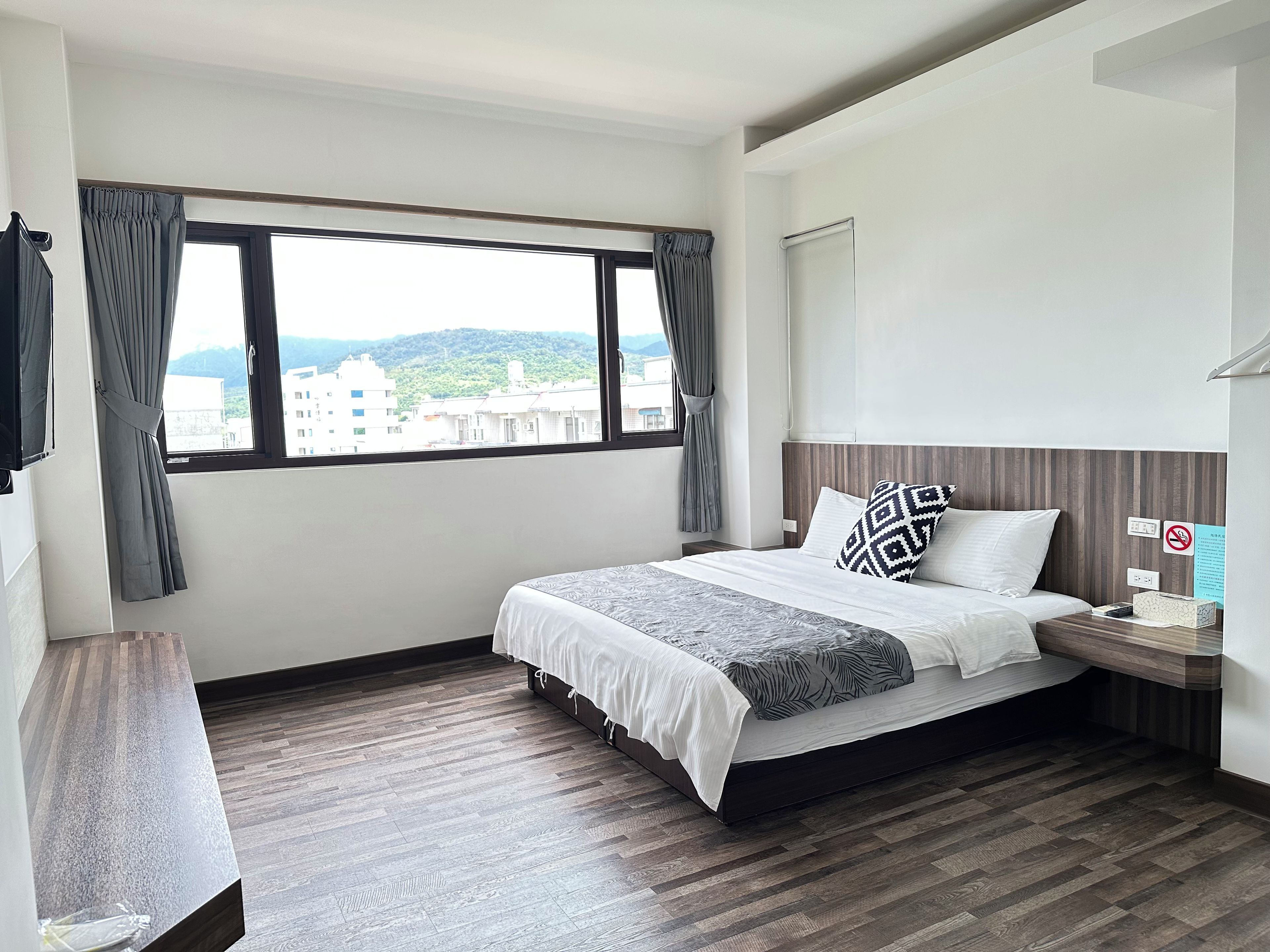A hotel room with a bed, bedside table, and a window with curtains.
