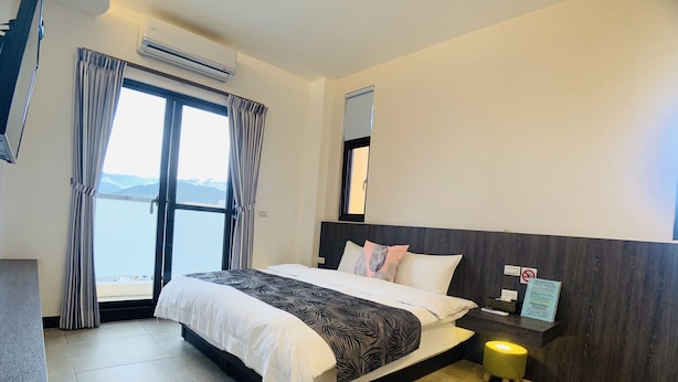 A hotel room with a large bed, a nightstand, a mirror, and a view of the sea. - Xuyu B&B (Chishang)