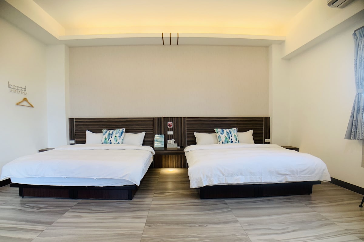 A hotel room with two beds, a wooden headboard, a wall-mounted air conditioner, and a hanging garment rack.