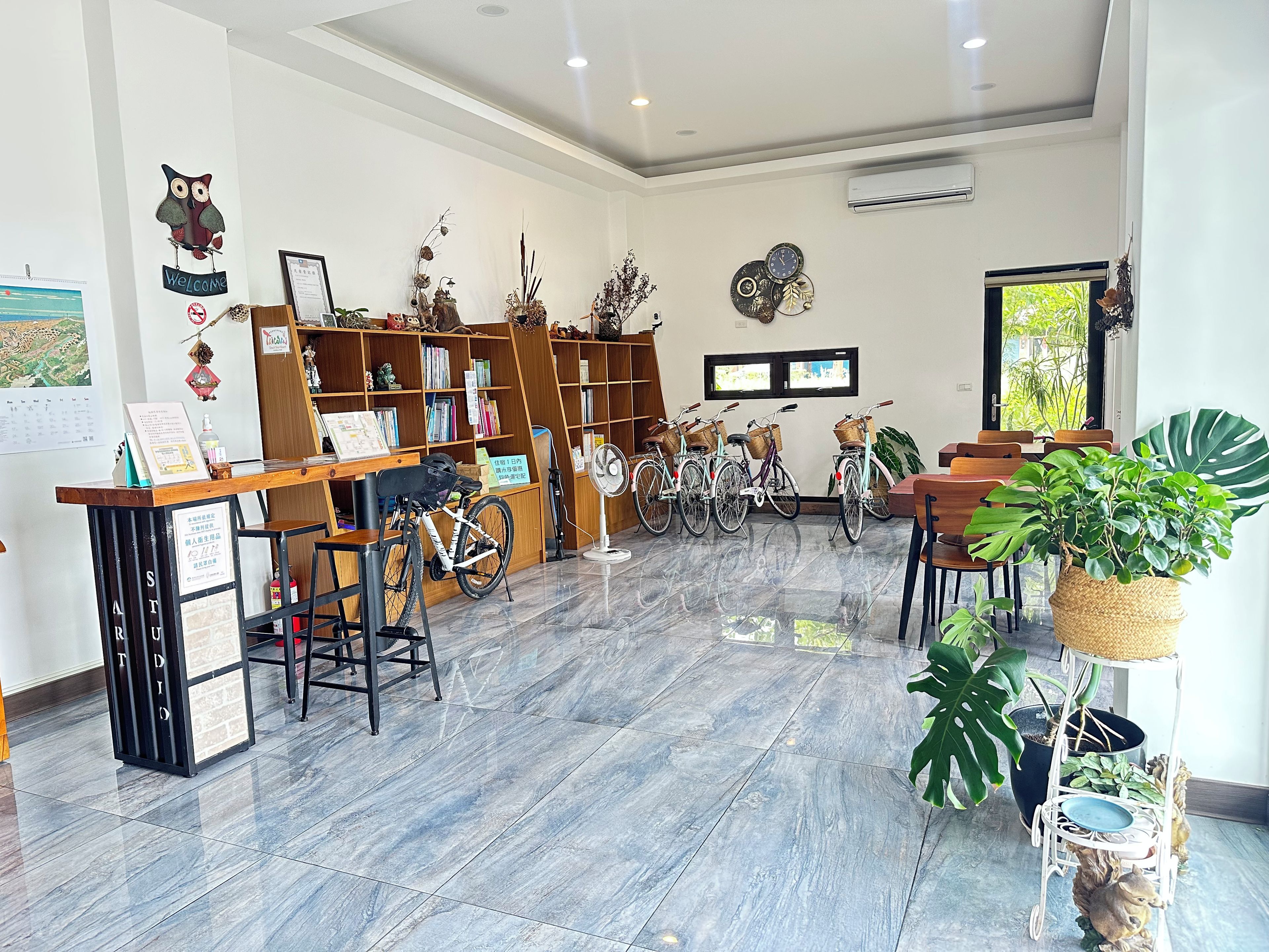 A library with bookshelves, a reception desk, bicycles, and potted plants.