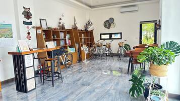 A library with bookshelves, a reception desk, bicycles, and potted plants.
