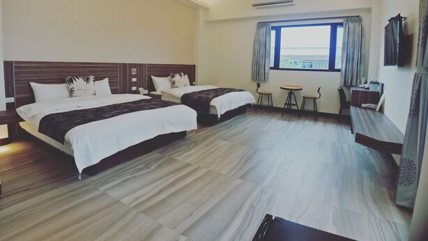 Habitación de hotel con dos camas, una mesita, sillas, televisión y ventana con cortinas.