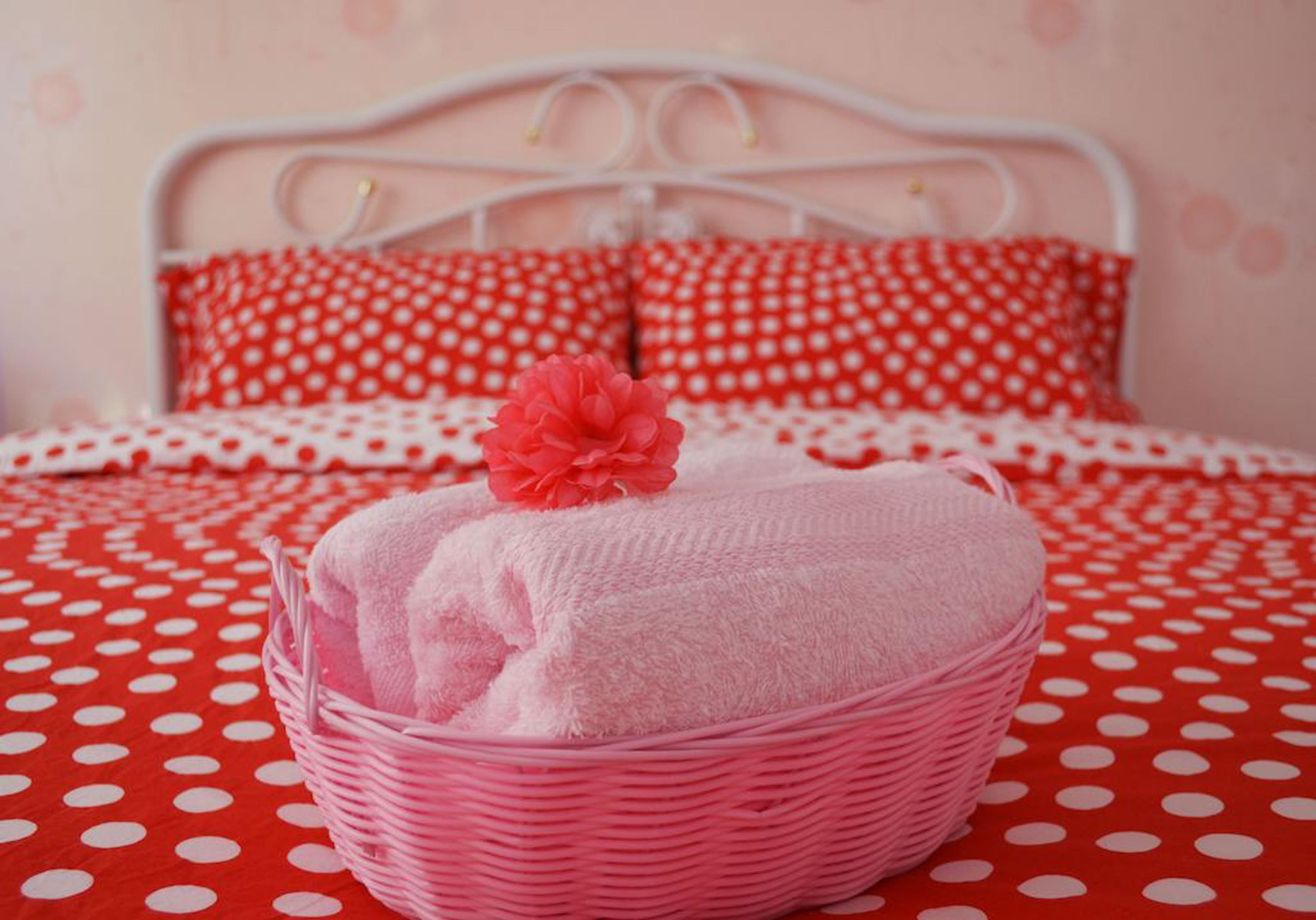 A bed with a red polka dot bedspread, a white metal headboard, and two red pillows with white polka dots.