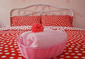 A bed with a red polka dot bedspread, a white metal headboard, and two red pillows with white polka dots.