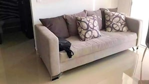 Ein beiges Sofa mit gemusterten Kissen in einem gut beleuchteten Raum mit Fliesenboden.
