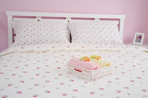 A bed with a floral patterned bedspread, white pillows with a small floral design, and a white bedside table with a picture frame. - Manis-Manis Cottage Lodge (Malacca City)