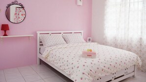 Un dormitorio con temática rosa, que incluye una cama blanca, ropa de cama floral, una lámpara roja, un espejo redondo y un estante pequeño.