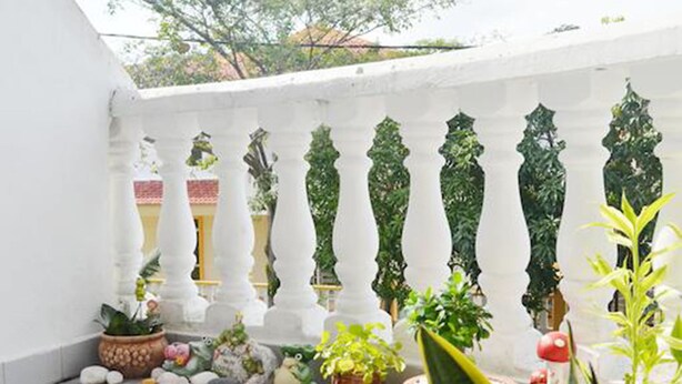 Un balcón con barandas blancas, plantas en macetas y piso de baldosas.