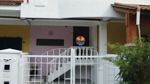 Un edificio de dos pisos con un balcón blanco y una entrada protegida por una reja.