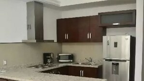 A modern kitchen with a central island, bar stools, a stainless steel refrigerator, and a microwave. - Condo Campo G (Mazatlán)