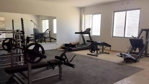 A gym with various exercise equipment, large windows, and a mirror. - Condo Campo G (Mazatlán)