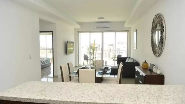 A spacious living area with a dining table and chairs, a sofa, and a balcony with a view. - Condo Campo G (Mazatlán)