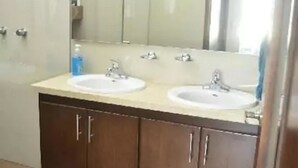 A bathroom with two sinks, a large mirror, and wooden cabinets. - Condo Campo G (Mazatlán)