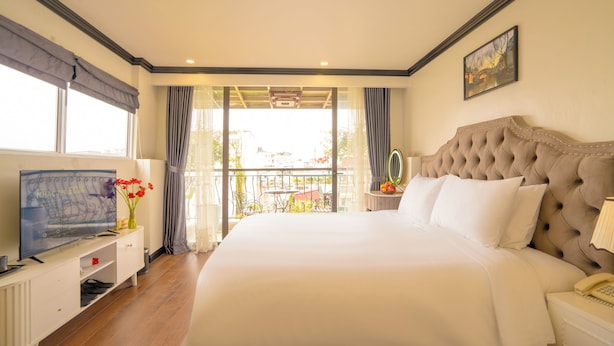 A hotel room with a large bed, a television, a bedside table with a lamp, and a view of the outdoors through a balcony.