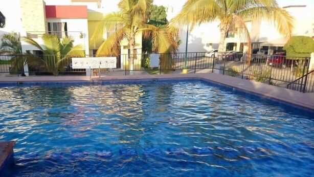 Una piscina con agua cristalina azul, rodeada por una valla y palmeras.