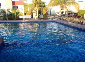 A swimming pool with clear blue water, surrounded by a fence and palm trees. - Casa A (Mazatlán)