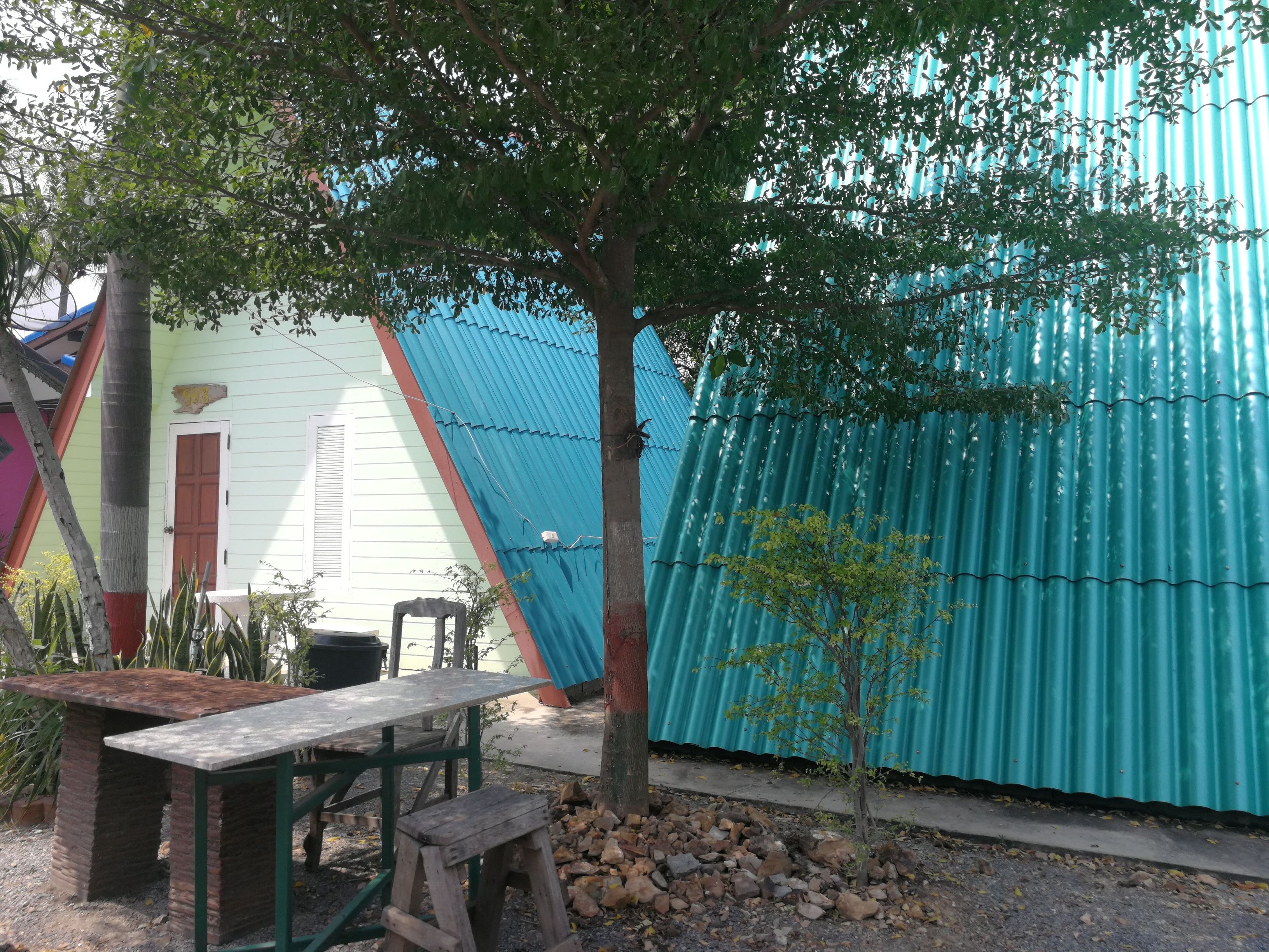 Un espacio de estar al aire libre de estilo rústico con una mesa de madera y bancos, rodeado de árboles y una valla de metal corrugado.