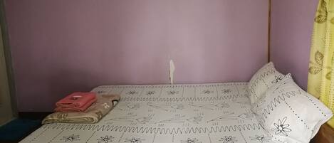 Un lit avec un motif floral, une serviette rose et un oreiller blanc orné d’un motif de feuilles.