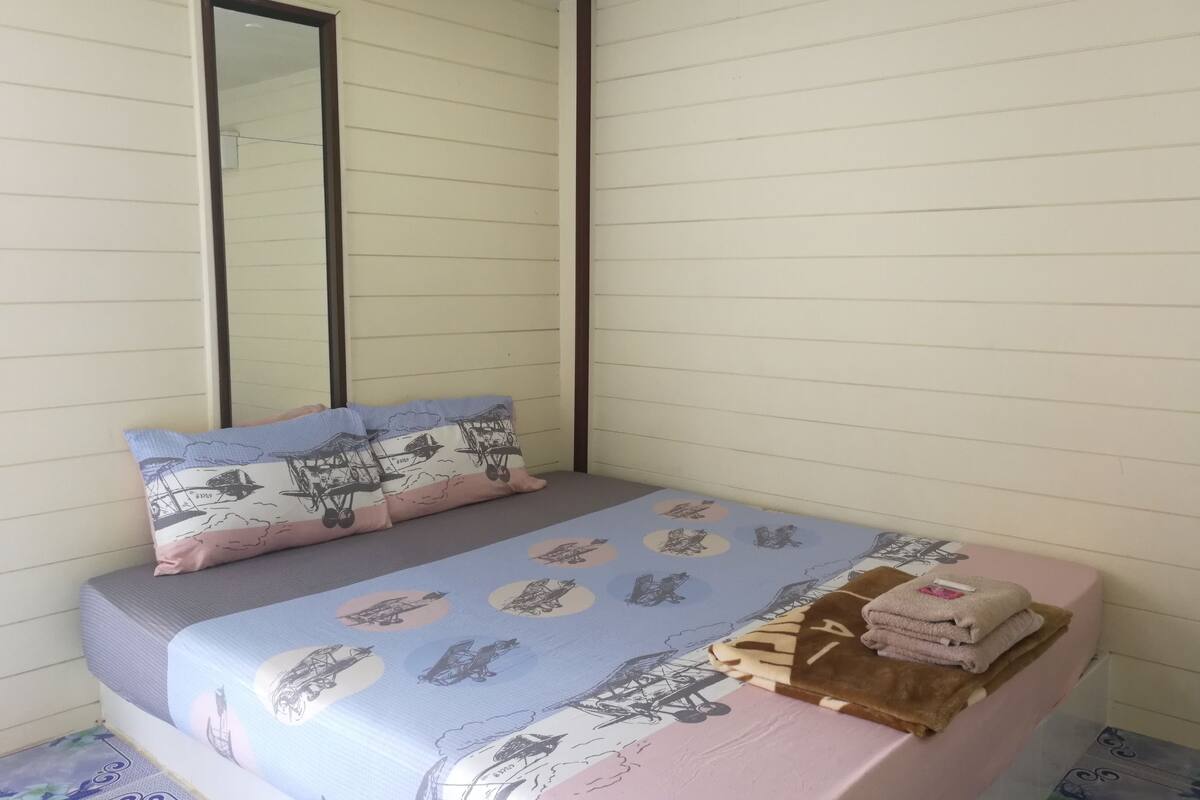 A bed with a patterned bedspread, pillows, and a stack of folded towels.