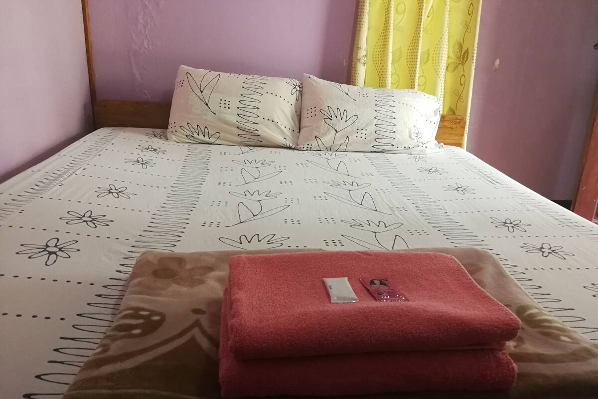 A bed with a patterned bedspread, a pillow, and a folded towel.