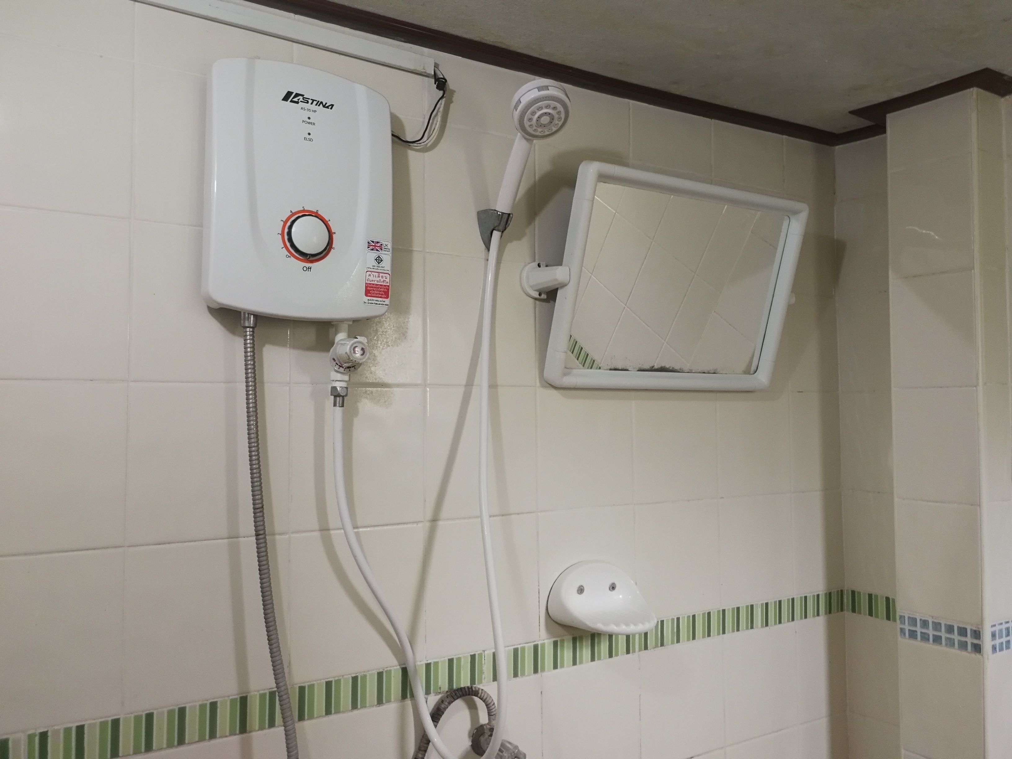 A bathroom with a wall-mounted water heater, a showerhead, and a small window.