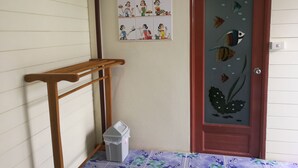 Una esquina de una habitación con un banco de madera, un cubo de basura, una puerta decorada con motivos de peces y una pared con un póster de temática familiar.
