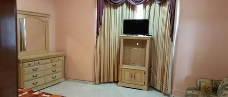 A bedroom with a bed, a dresser, a TV on a stand, and a patterned rug.