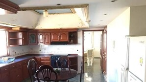 A kitchen with wooden cabinets, a dining table with chairs, and a refrigerator. - Casa Cid (Mazatlán)
