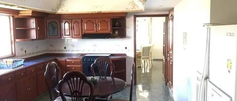A kitchen with wooden cabinets, a dining table with chairs, and a refrigerator.