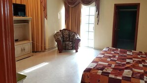 A bedroom with a bed, a chair, a TV on a shelf, and a wardrobe. - Casa Cid (Mazatlán)