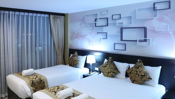 Habitación de hotel con dos camas, una mesita de noche, una lámpara y una pared con diseños geométricos y florales.