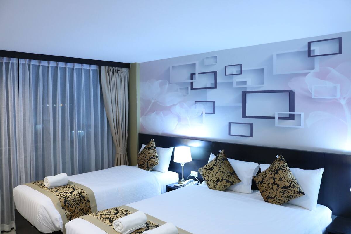 A hotel room with two beds, a nightstand, a lamp, and a wall with geometric and floral designs.