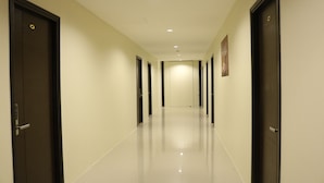 Un pasillo largo y estrecho con puertas oscuras a ambos lados, que conduce a una habitación luminosa al final.