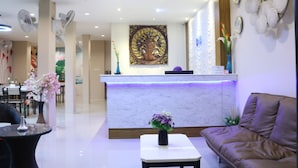Zona de recepción de hotel con un mostrador de mármol, un reloj grande en la pared y una lámpara moderna en el techo.