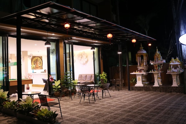 An outdoor seating area with tables and chairs, a covered section with a glass wall, and a decorative shrine.
