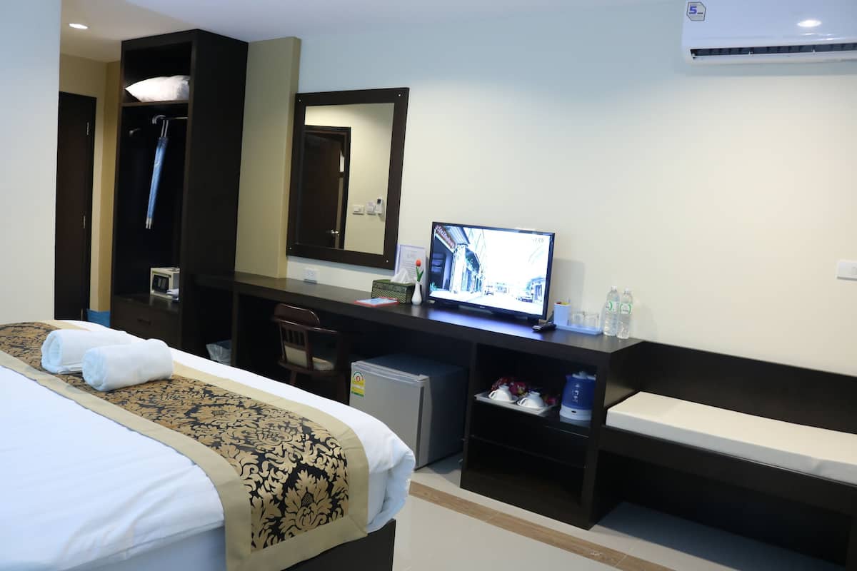 A hotel room with a bed, a desk, a television, a mirror, a small refrigerator, and a bench.