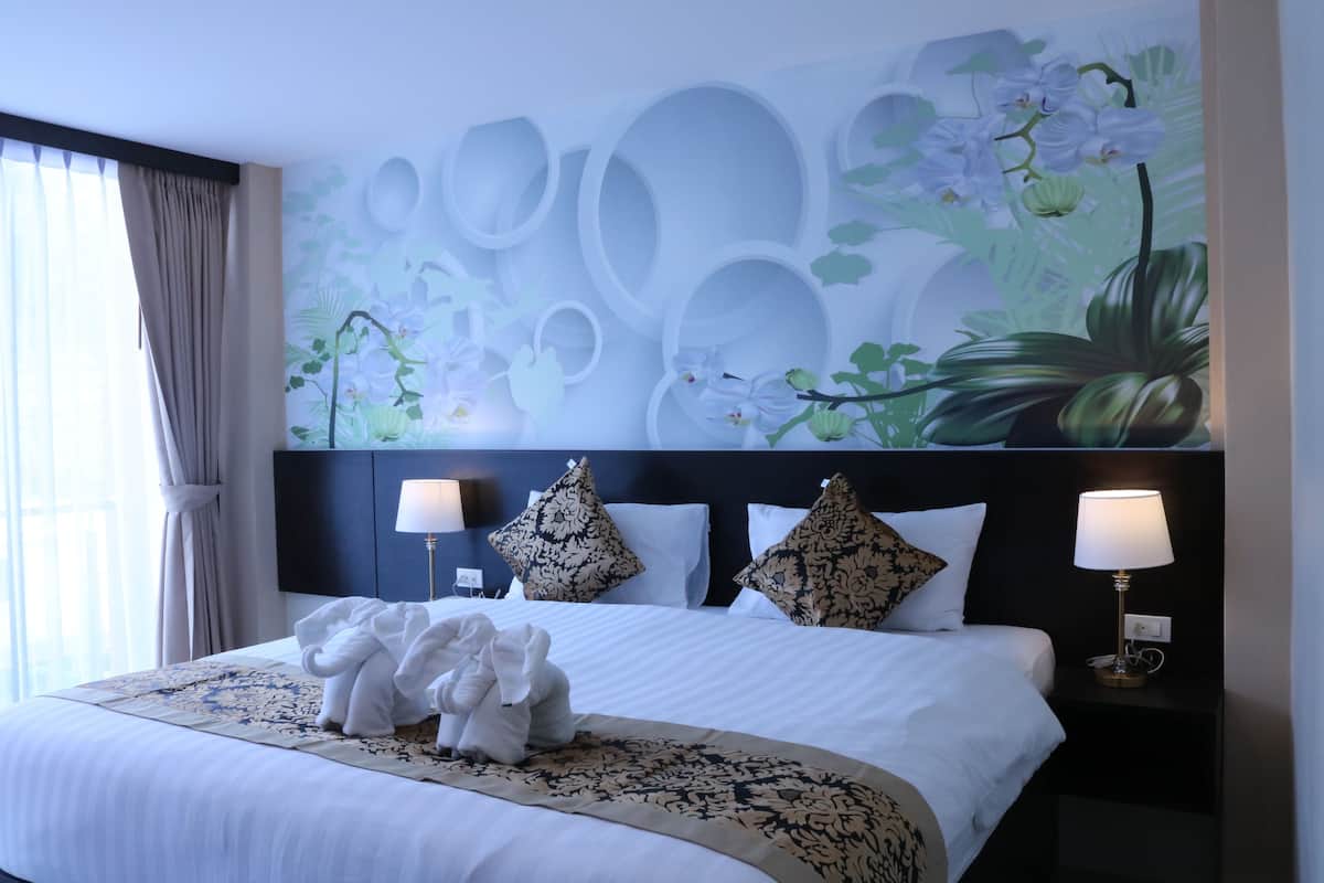 A hotel room with a large bed, two bedside lamps, a headboard with a floral mural, and a window with curtains.