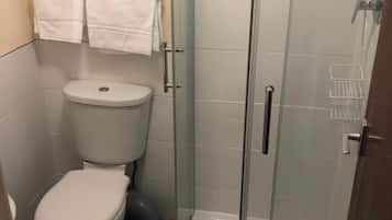 Un baño pequeño con inodoro, ducha con cerramiento de vidrio y piso de baldosas.
