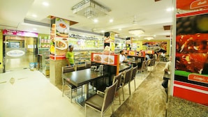 A restaurant with multiple dining tables and chairs, a food display counter, and a ceiling fan. - Sriram International (Coimbatore)