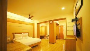 A hotel room with a wooden bed, a bedside table, a clock, and a television mounted on the wall. - Sriram International (Coimbatore)