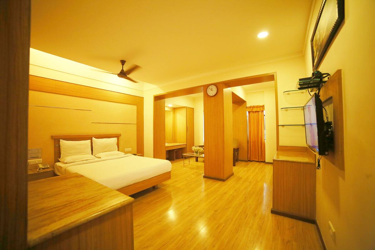 Una habitación de hotel con una cama de madera, una mesita de noche, un reloj y un televisor fijado a la pared.