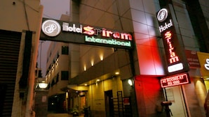 The exterior of Hotel Sriram International with a neon sign, a visible entrance, and a sign indicating AC rooms at Rs 1500. - Sriram International (Coimbatore)