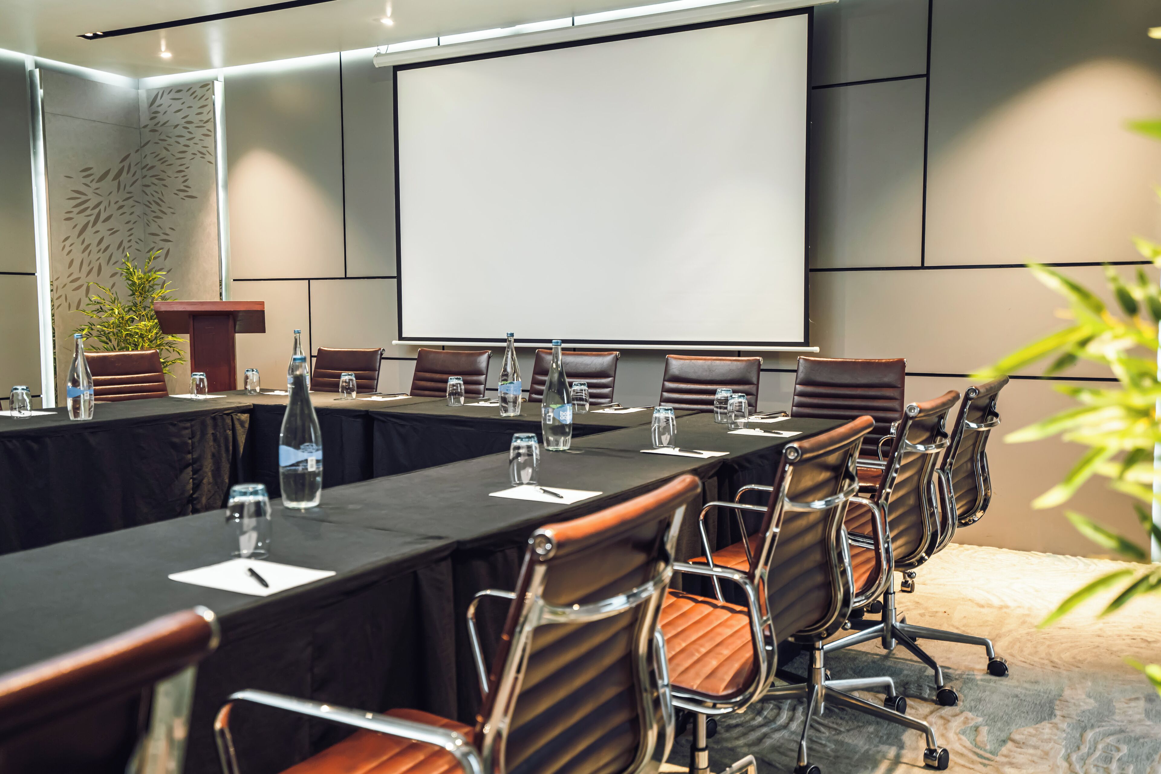 A conference room with a long table, chairs, a projector screen, and a podium.