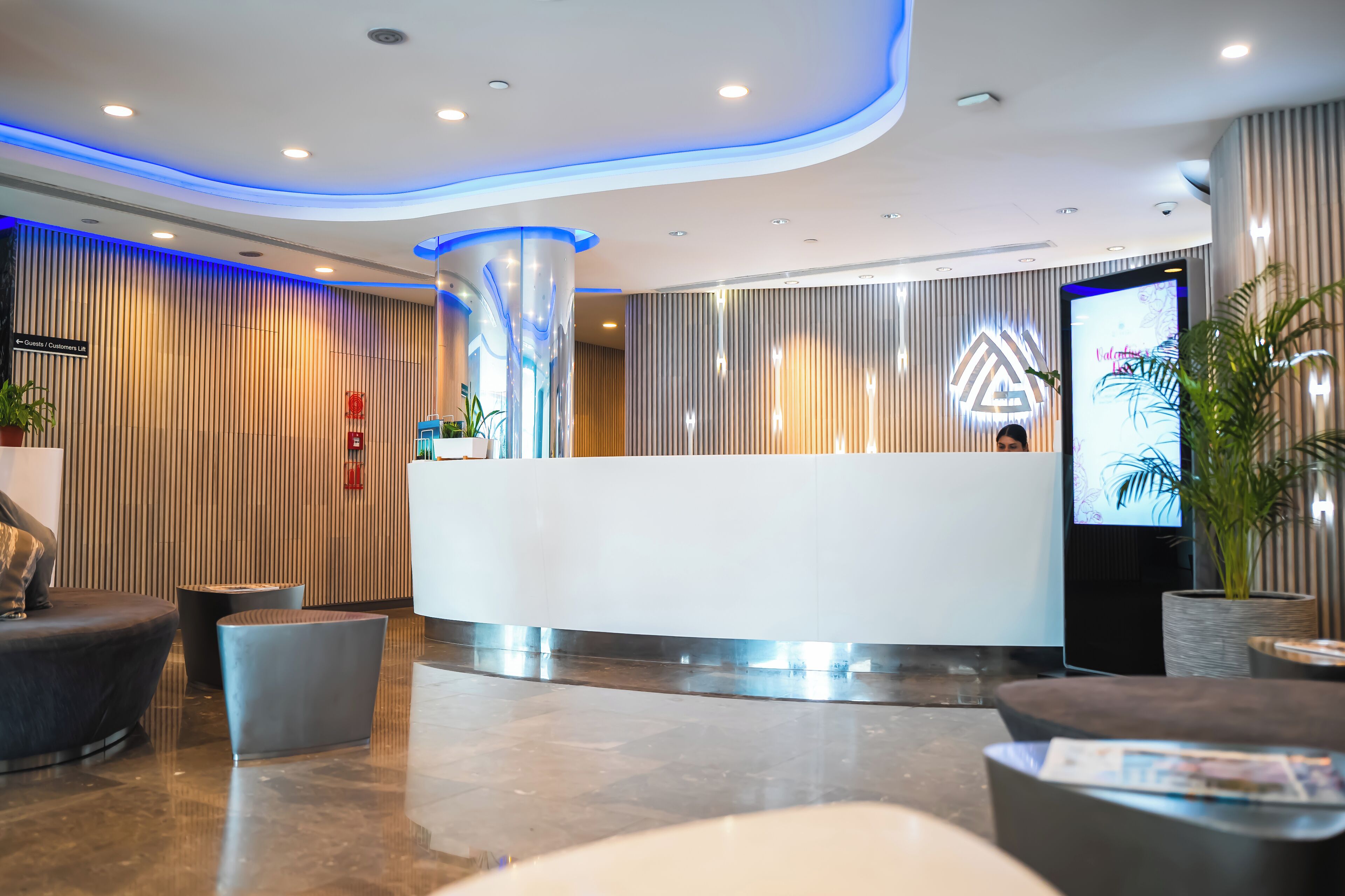 A modern reception area with a curved reception desk, a digital screen, and a potted plant.