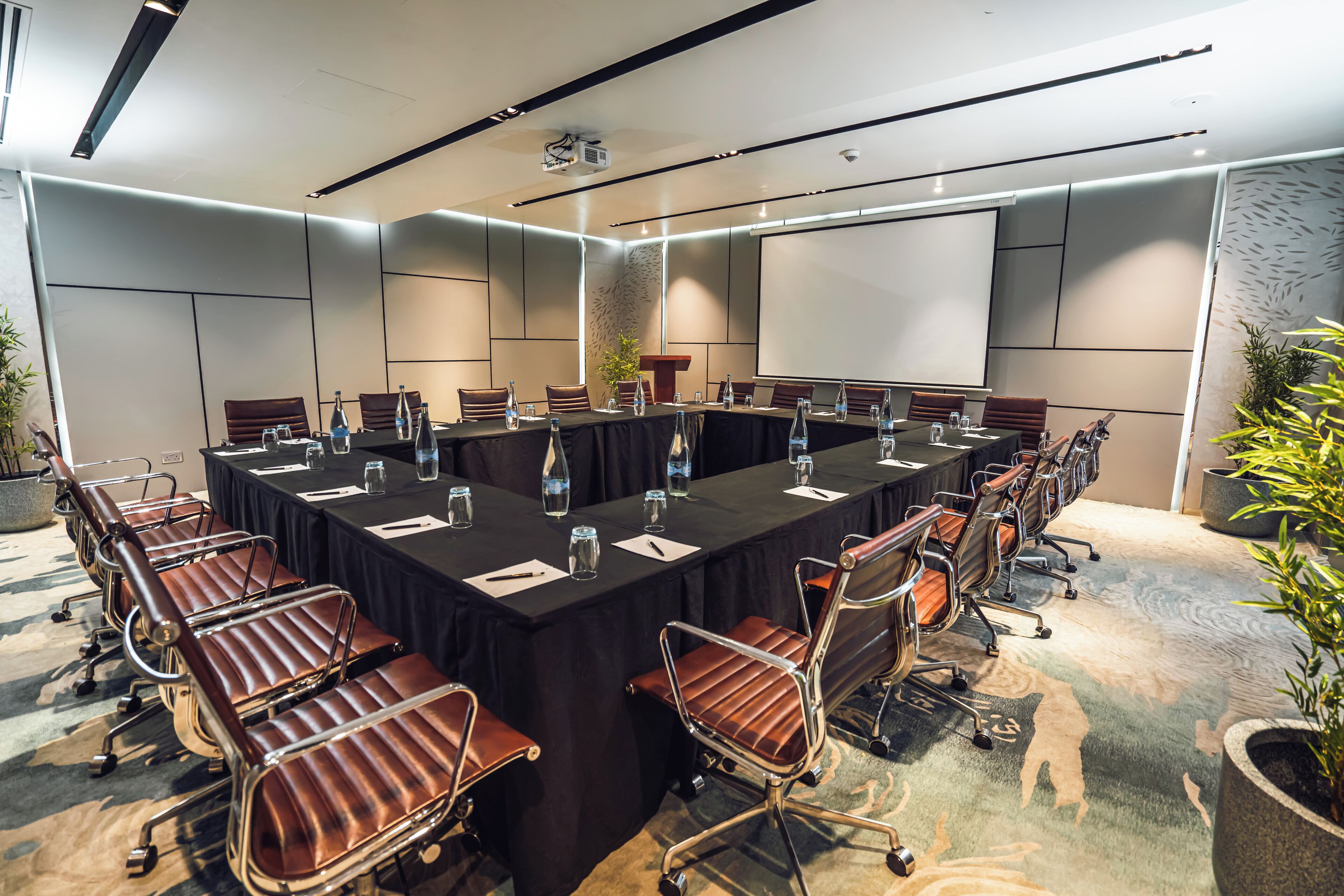 Una sala de conferencias con una mesa larga, varias sillas, botellas de agua y una pantalla de proyector.