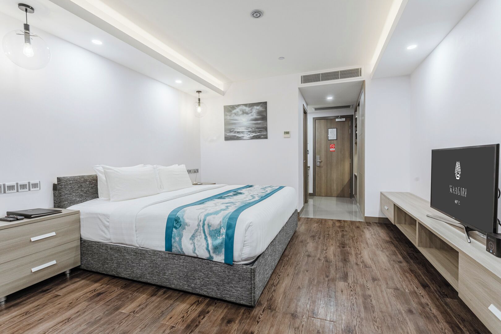 A modern hotel room with a large bed, a TV, a desk, and a painting on the wall.